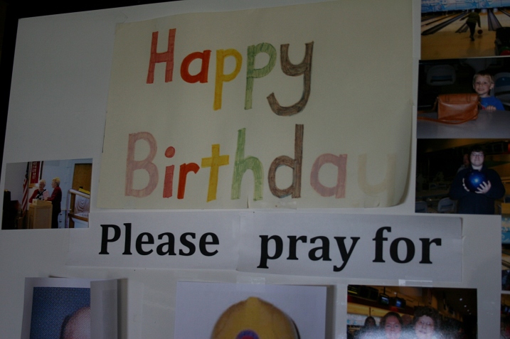 A poster board with photos and well wishes stands in the church entry.