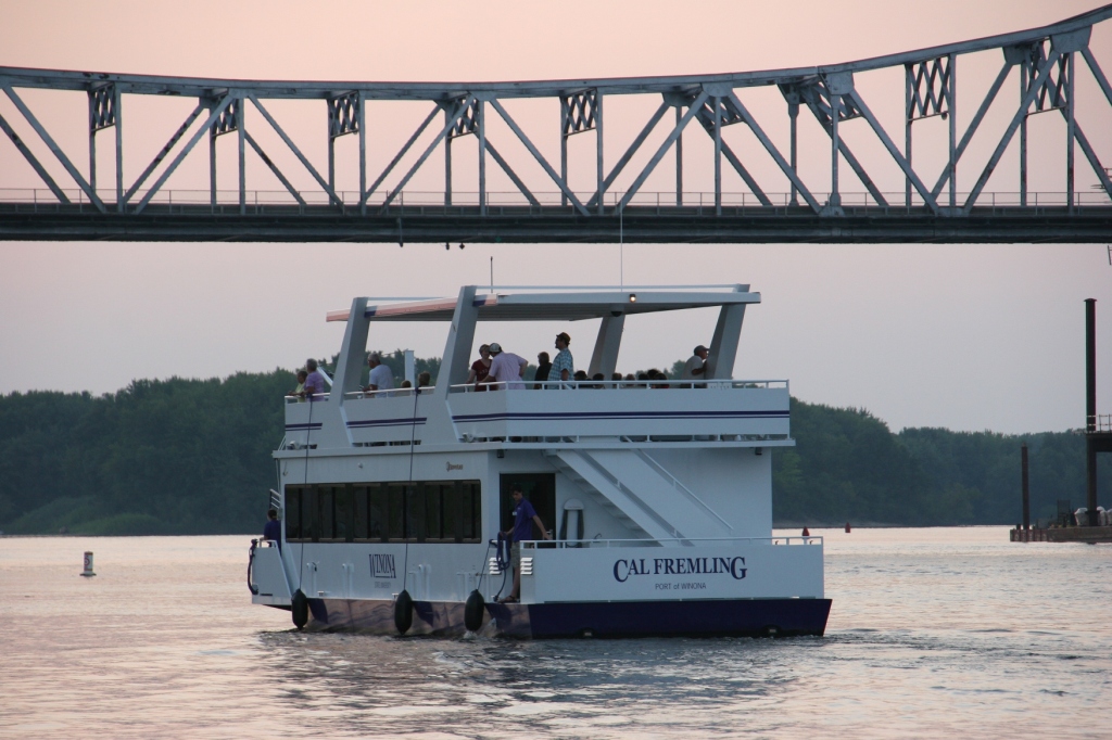 As the sun sets, Winona State University's Cal Fremling boat passes under the Mississippi Rover bridge in Winona. Minnesota Prairie Roots photo, September 2015.